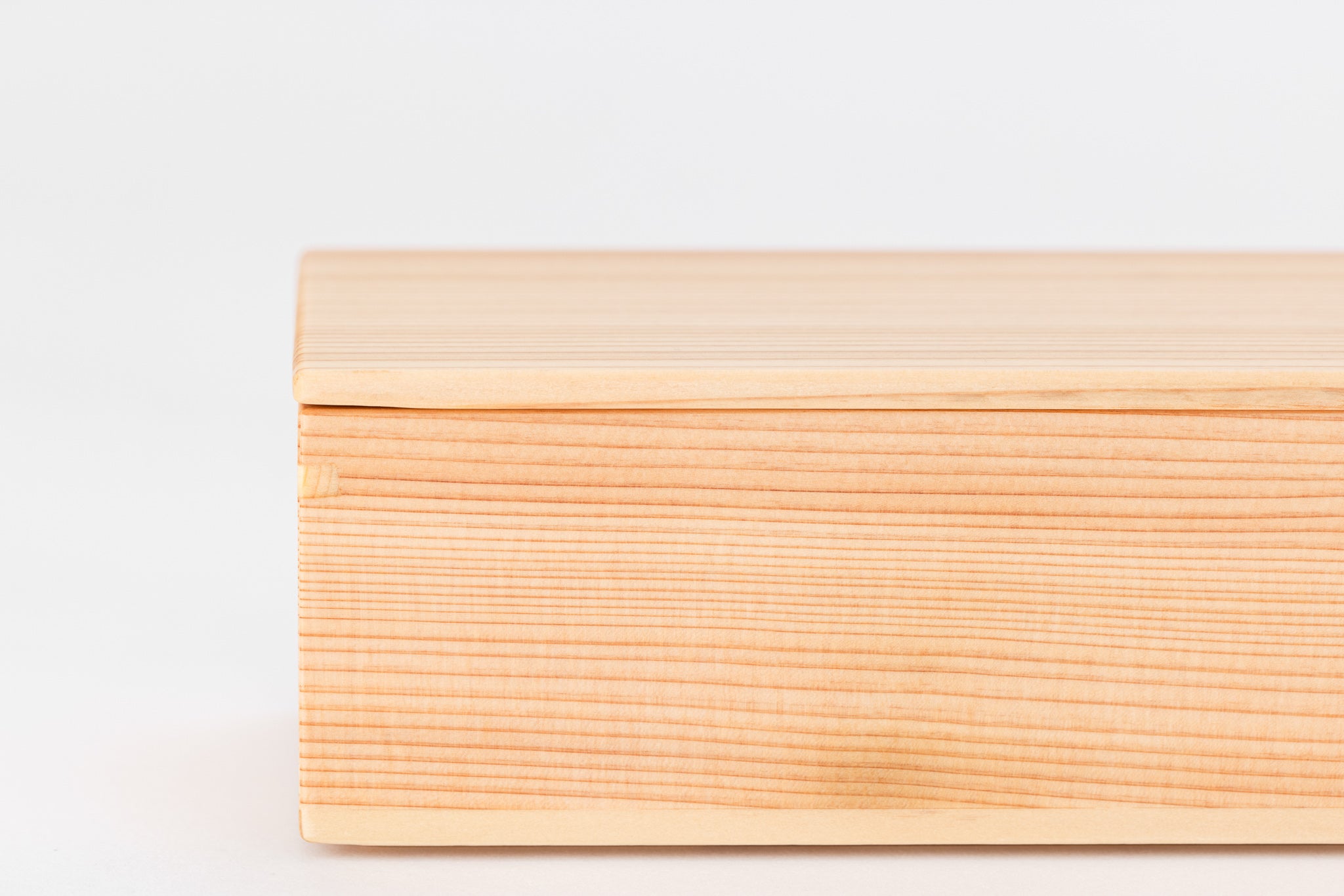 A closeup of a rectangular box made of light-colored cedar on a white background with its lid closed. The grain of the wood is very straight.