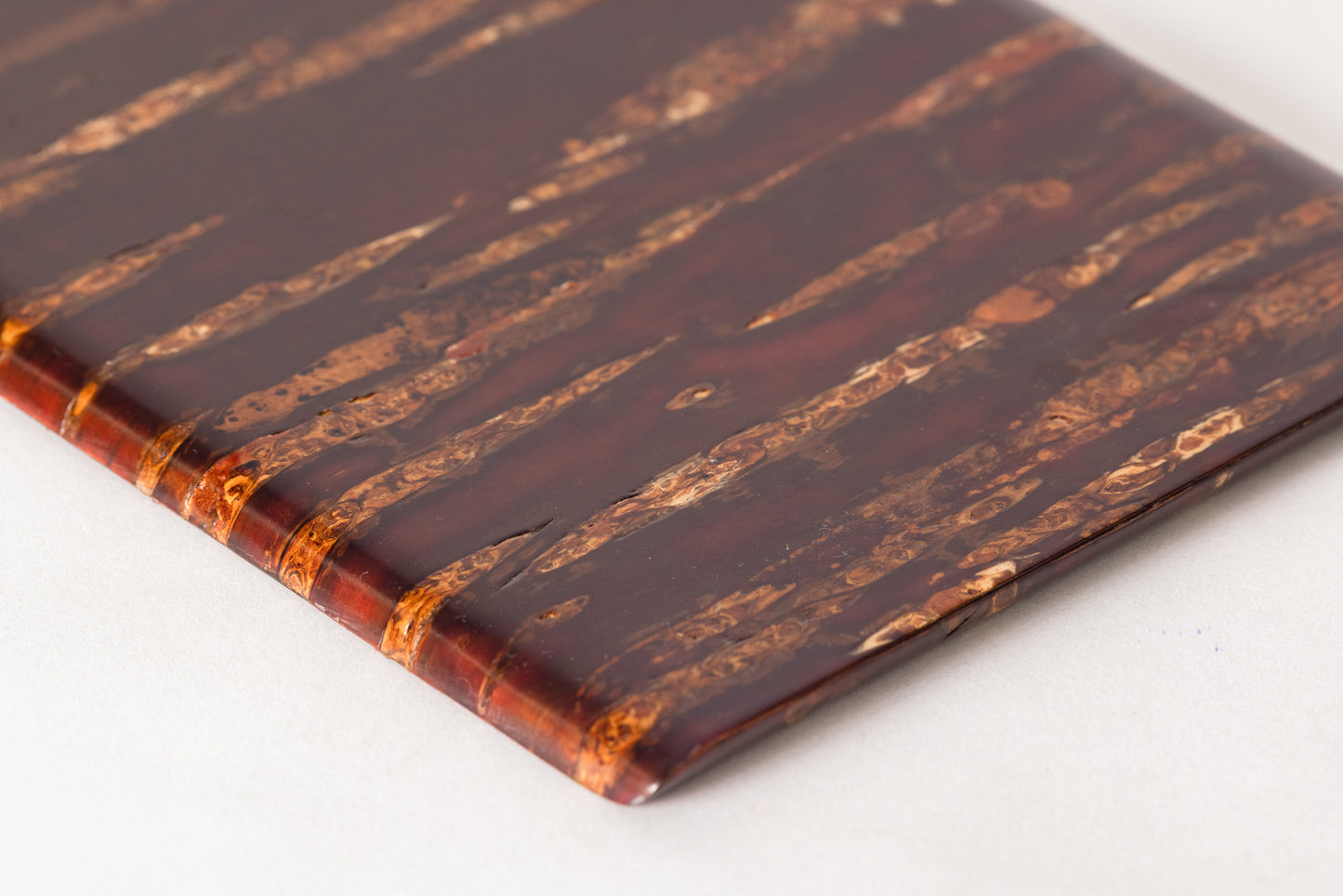 A close up of a  rectangular plate made of shiny red cherry bark on a plain white background. The cherry bark's natural pattern is deep red with stripes of orange. The plate is polished and shiny.