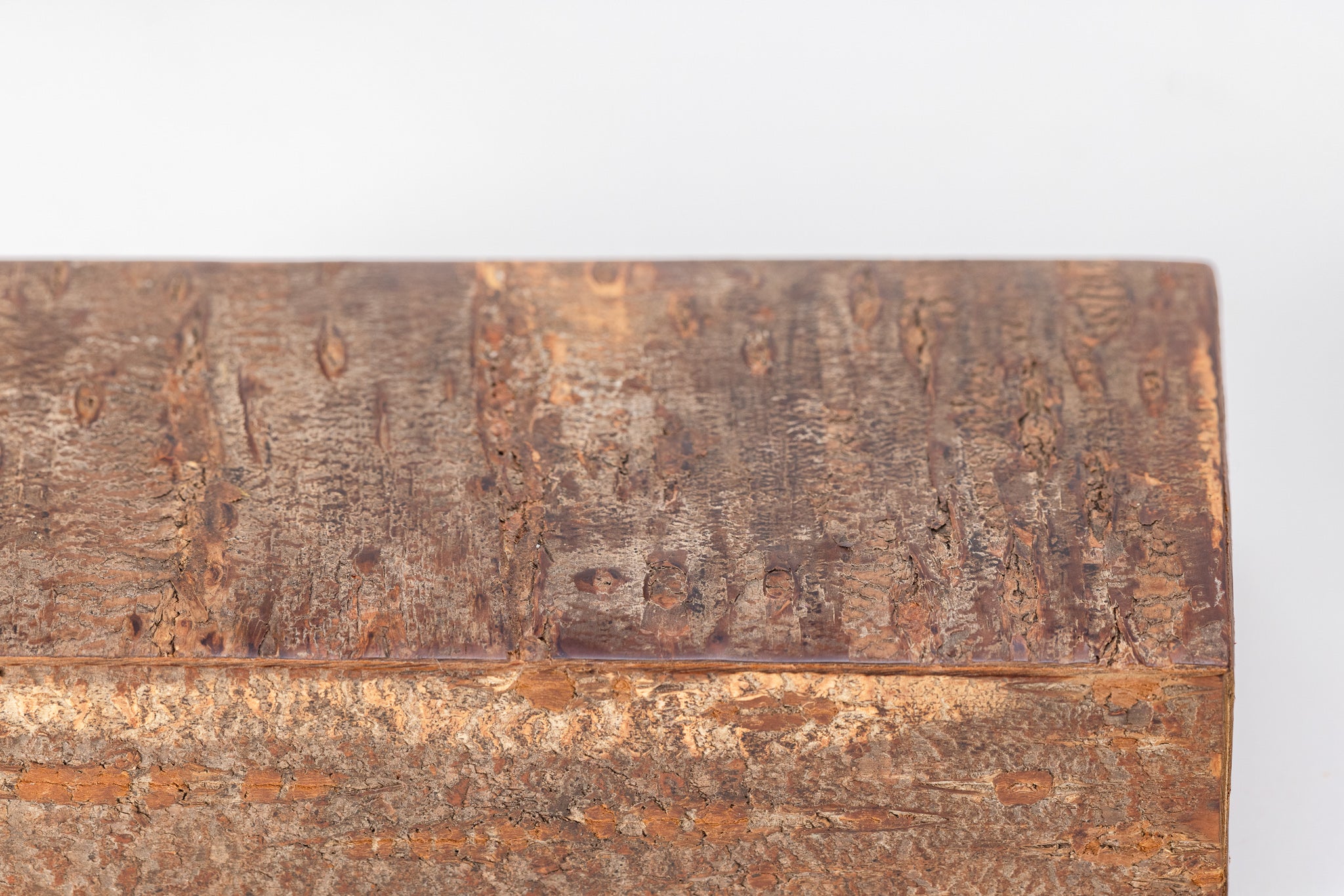 A close up of a rectangular wooden box made of cherry bark sits on a white background with its lid closed. The outside of the box is rough like the bark of a cherry tree and has a lot of texture.