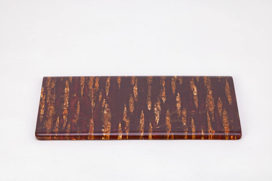 A rectangular wooden plate made of cherry bark on a plain white background.  The cherry bark's natural pattern is deep red with orange stripes. The bark is polished and shiny. The plate's long edge faces the viewer.
