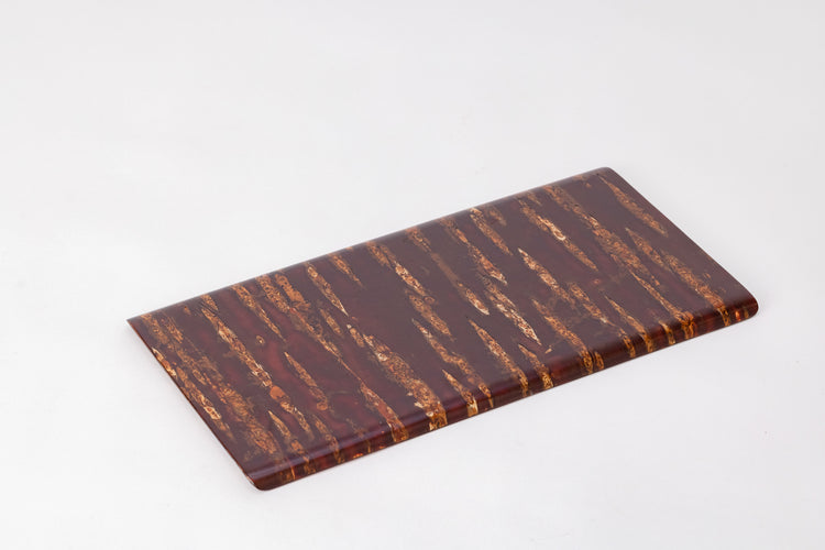 A rectangular wooden plate made of cherry bark on a plain white background.  The cherry bark's natural pattern is deep red with orange stripes. The bark is polished and shiny. The plate is angled diagonally from the viewer.